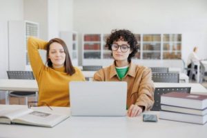 two women library coworking are sitting opposite each other working laptop scaled e1727355731370